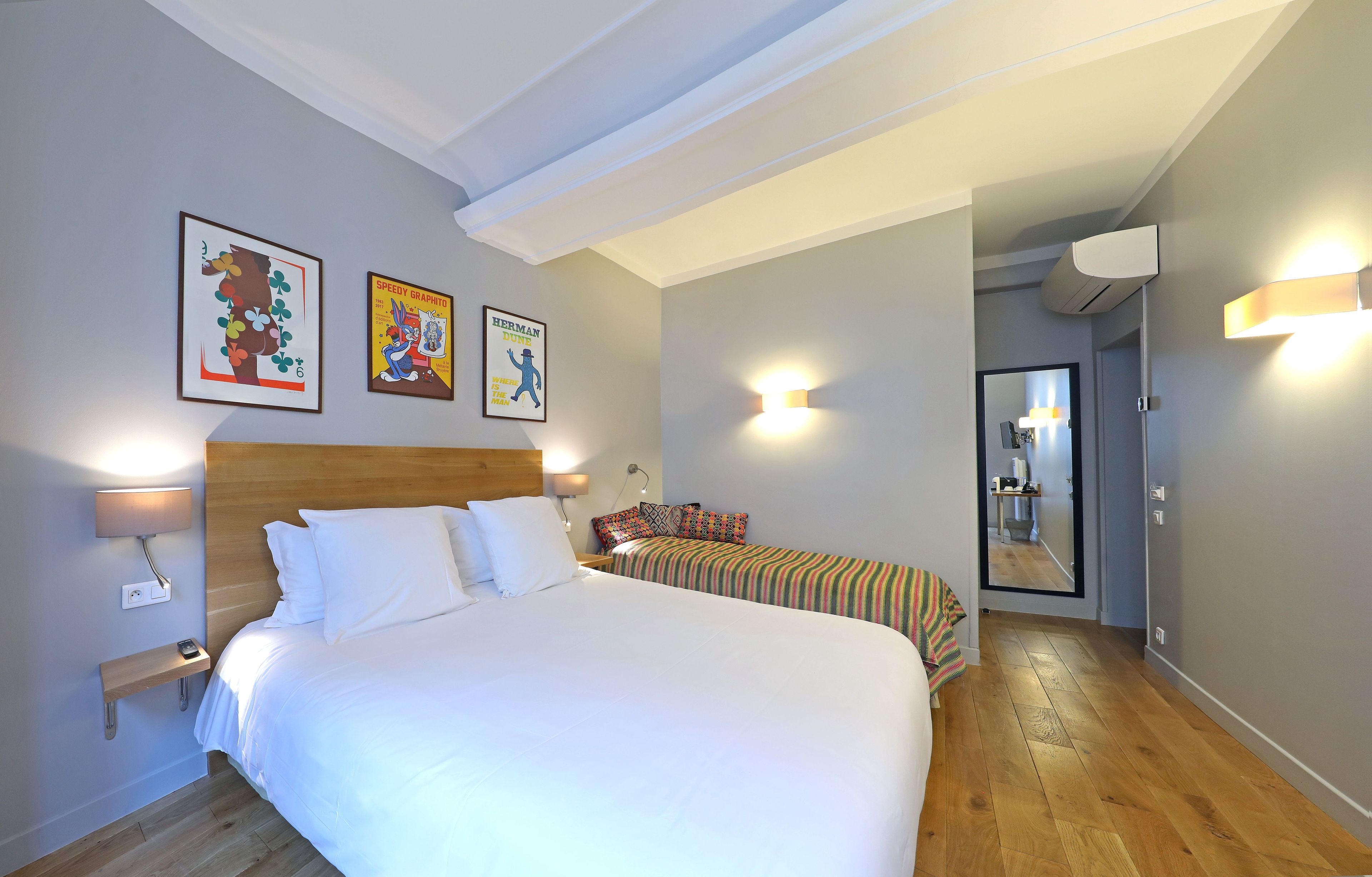 A hotel room with a large bed, bedside lamps, a small table, a mirror, and artwork on the wall.