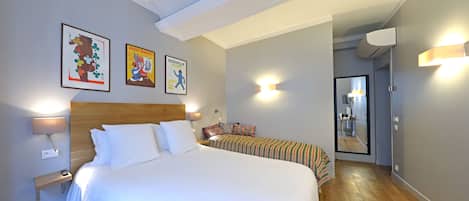 A hotel room with a large bed, bedside lamps, a small table, a mirror, and artwork on the wall.