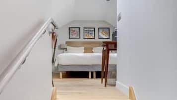 A staircase leading to a bedroom with a bed, a desk, and framed pictures on the wall.
