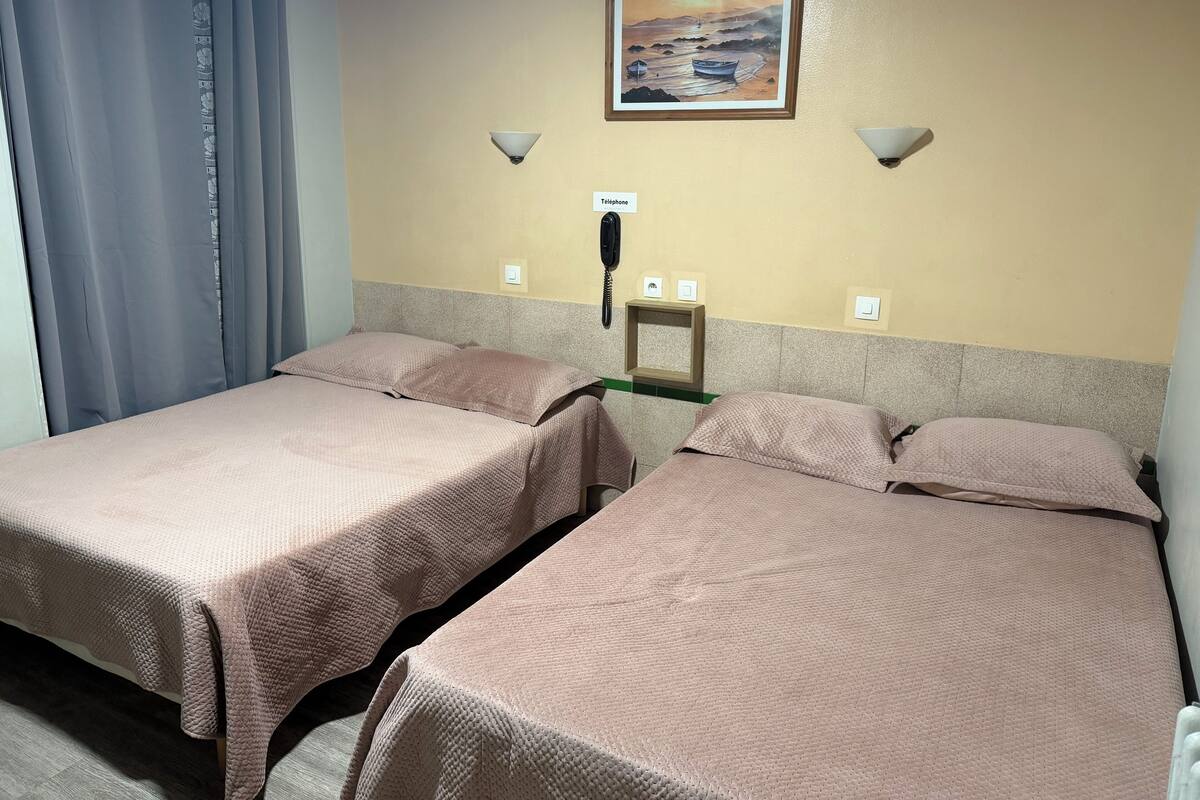 A hotel room with two beds, a painting on the wall, a telephone, and a light fixture.