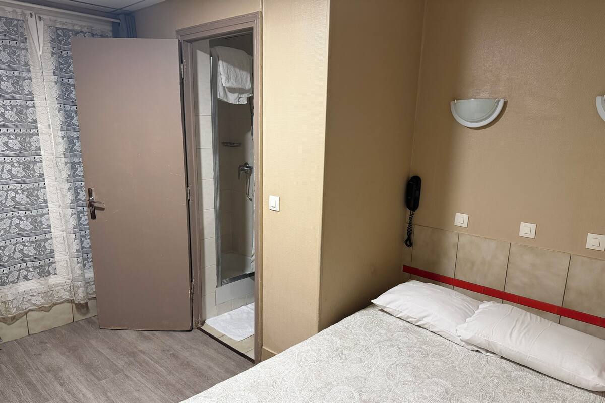 A hotel room with a bed, a shower, and a telephone.