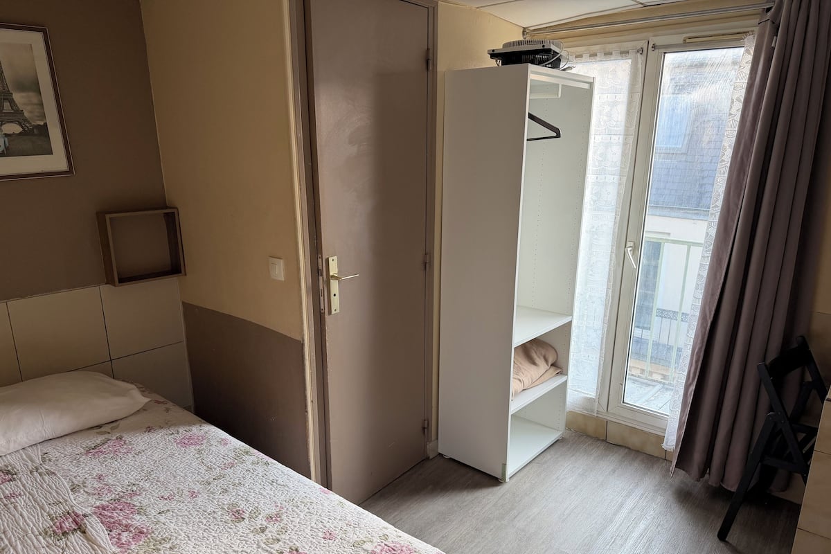 A bedroom with a bed, a wardrobe, a balcony with a view, and a framed picture on the wall.
