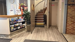 Un área de recepción con mostrador de madera, una planta en maceta, una escalera y una pared con un reloj y cuadros enmarcados.