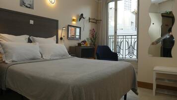 Quarto de hotel com cama grande, escrivaninha, cadeira, mesa pequena, espelho e varanda com guarda-corpo.