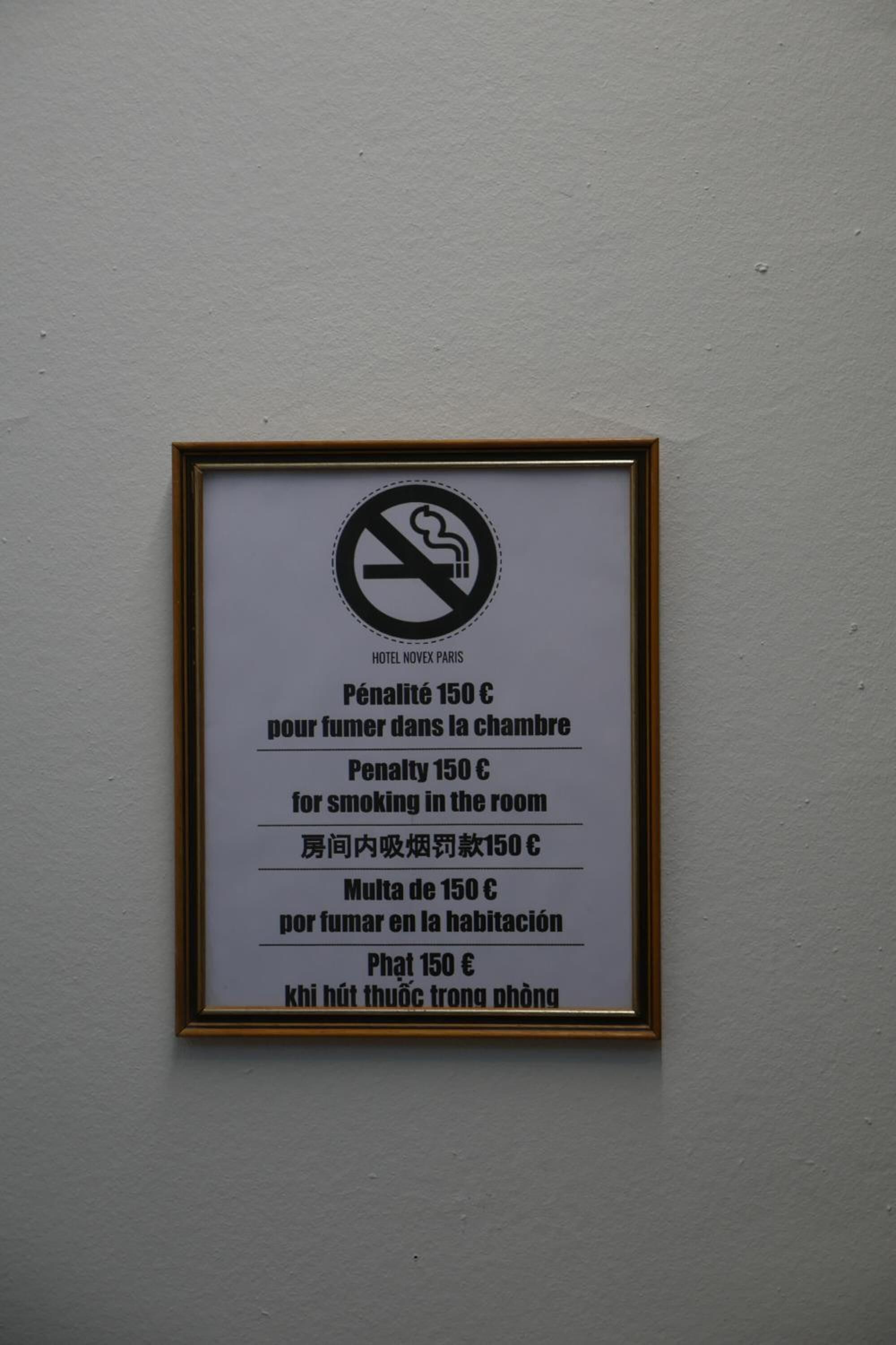 Placa emoldurada com símbolo de proibido fumar e texto em vários idiomas que indica multa por fumar no quarto.