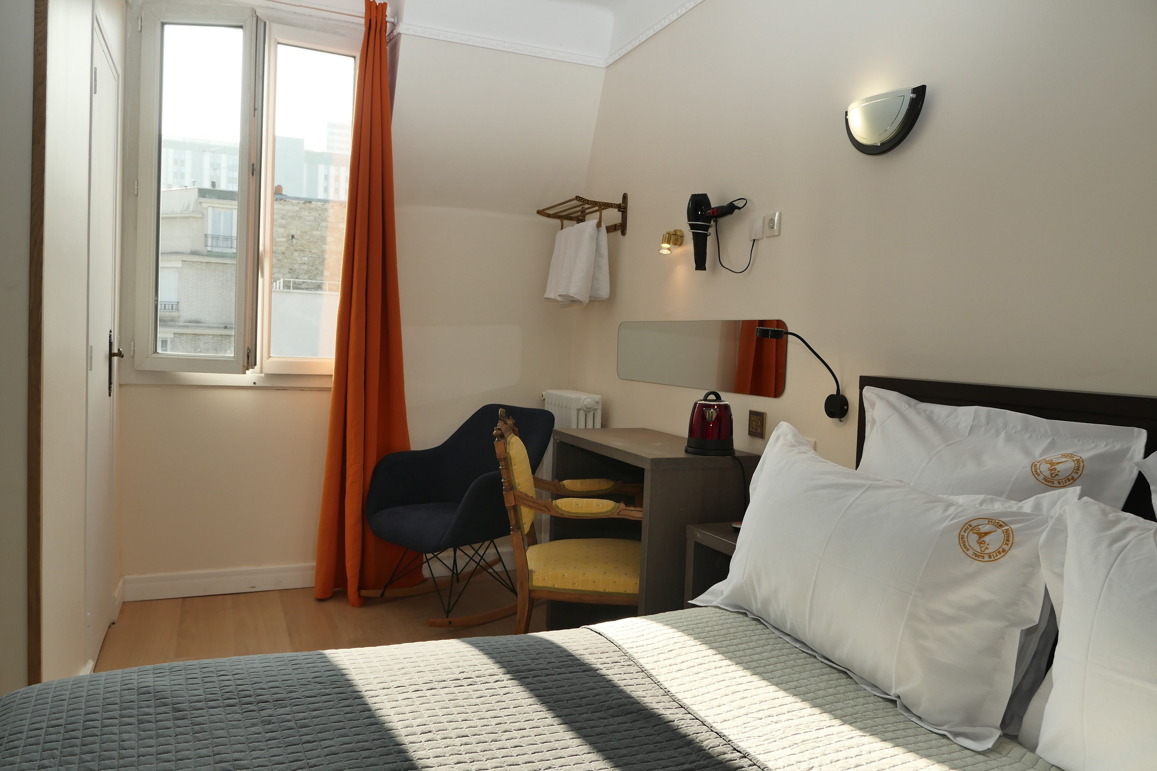 A hotel room with a bed, a desk, a chair, a window with curtains, and a wall-mounted mirror.