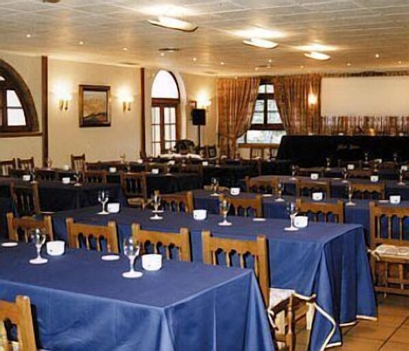 A banquet hall with tables set for dining, a piano, and a large arched window.