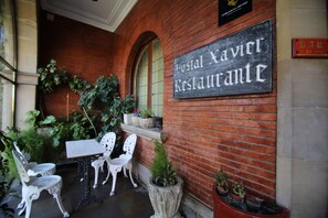 A brick building with a sign reading "Frontal Xavier Restaurant". There are white chairs and potted plants outside.