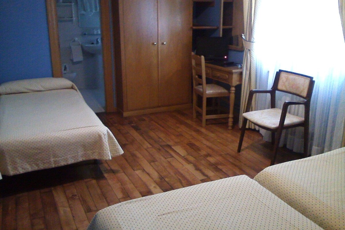 Een slaapkamer met twee bedden, een houten bureau, een stoel en een kledingkast.