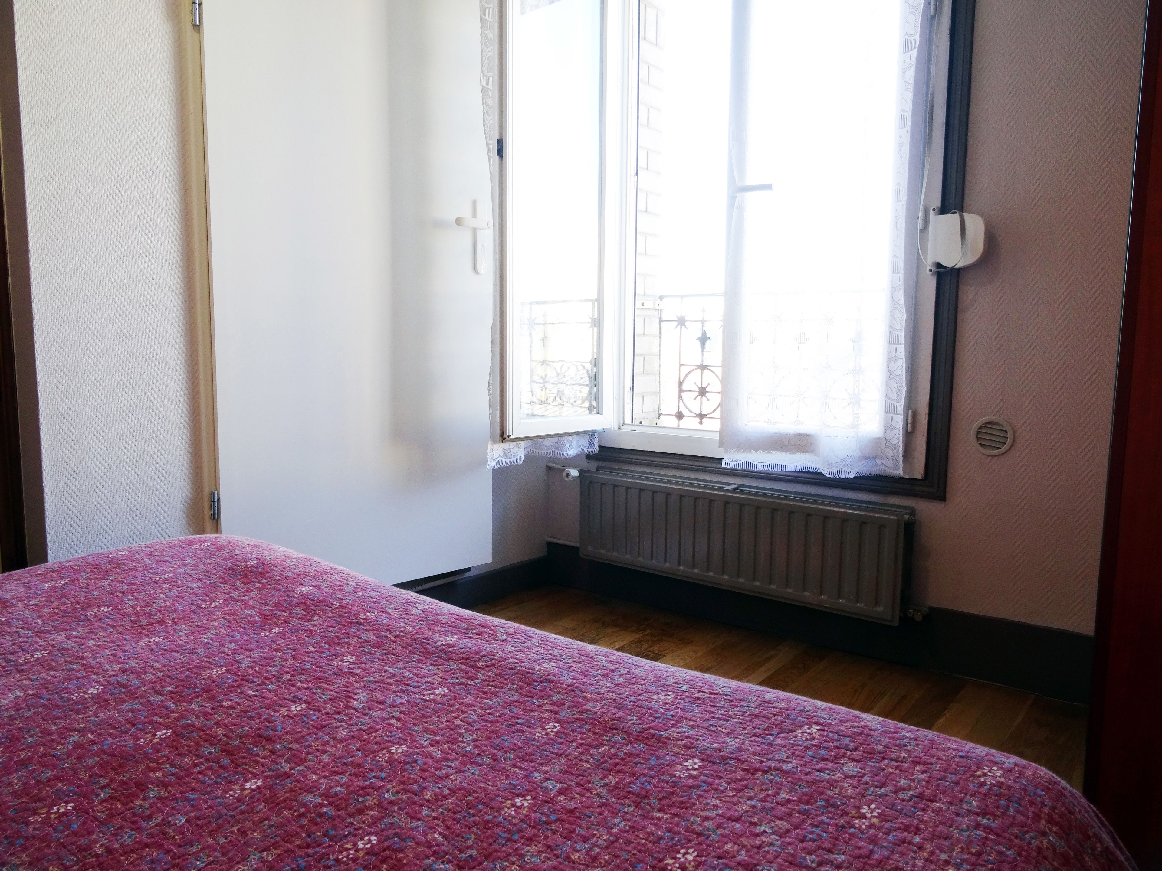 A bedroom with a bed, a window with a view of a balcony, and a radiator.