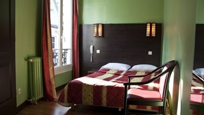 Een kamer met een bed, een stoel, een radiator, een raam met gordijnen en een aan de muur bevestigde telefoon.