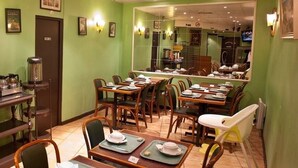 Een restaurant met groene muren, houten tafels en stoelen. Op de tafels staan verschillende items, zoals borden, kopjes en een koffieapparaat.