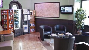 Een receptiehal met een automaat, zithoek en een televisiescherm.