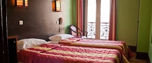 A room with two beds, a chair, a phone, and a window with a view of a balcony. - Hotel Cambrai (Paris)