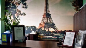 Een receptiebalie met een poster van de Eiffeltoren, een ingelijst certificaat, een blauwe container en een ingelijst menu.