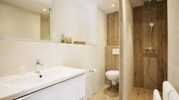 Un baño moderno con lavamanos blanco, espejo y zona de ducha con paneles de madera.