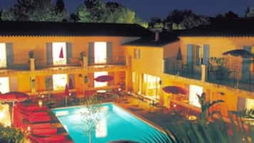 Un edificio de dos plantas con piscina, mobiliario exterior y un patio cubierto.