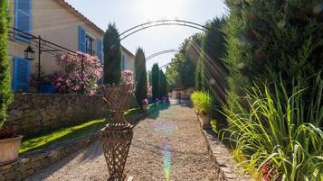 A gravel pathway leading to a house with a stone wall and potted plants.
