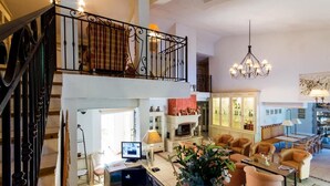 A spacious living area with a high ceiling, a fireplace, and a balcony with a railing.