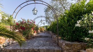 A stone pathway leading through a garden with archways and hanging lanterns.