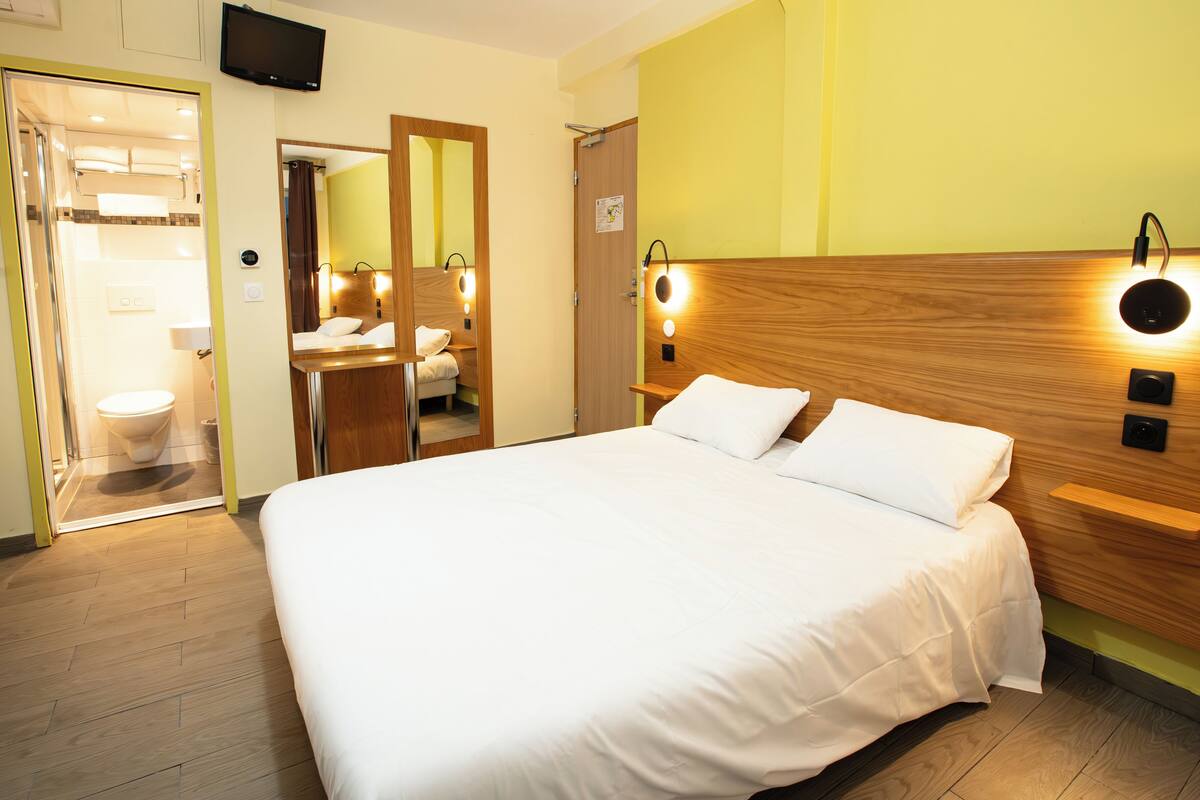 Une chambre d’hôtel avec un grand lit, une tête de lit en bois, des tables de chevet, un miroir et un téléviseur.
