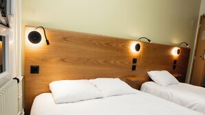 Habitación de hotel con dos camas, cabecero de madera y lámparas de lectura fijadas a la pared.