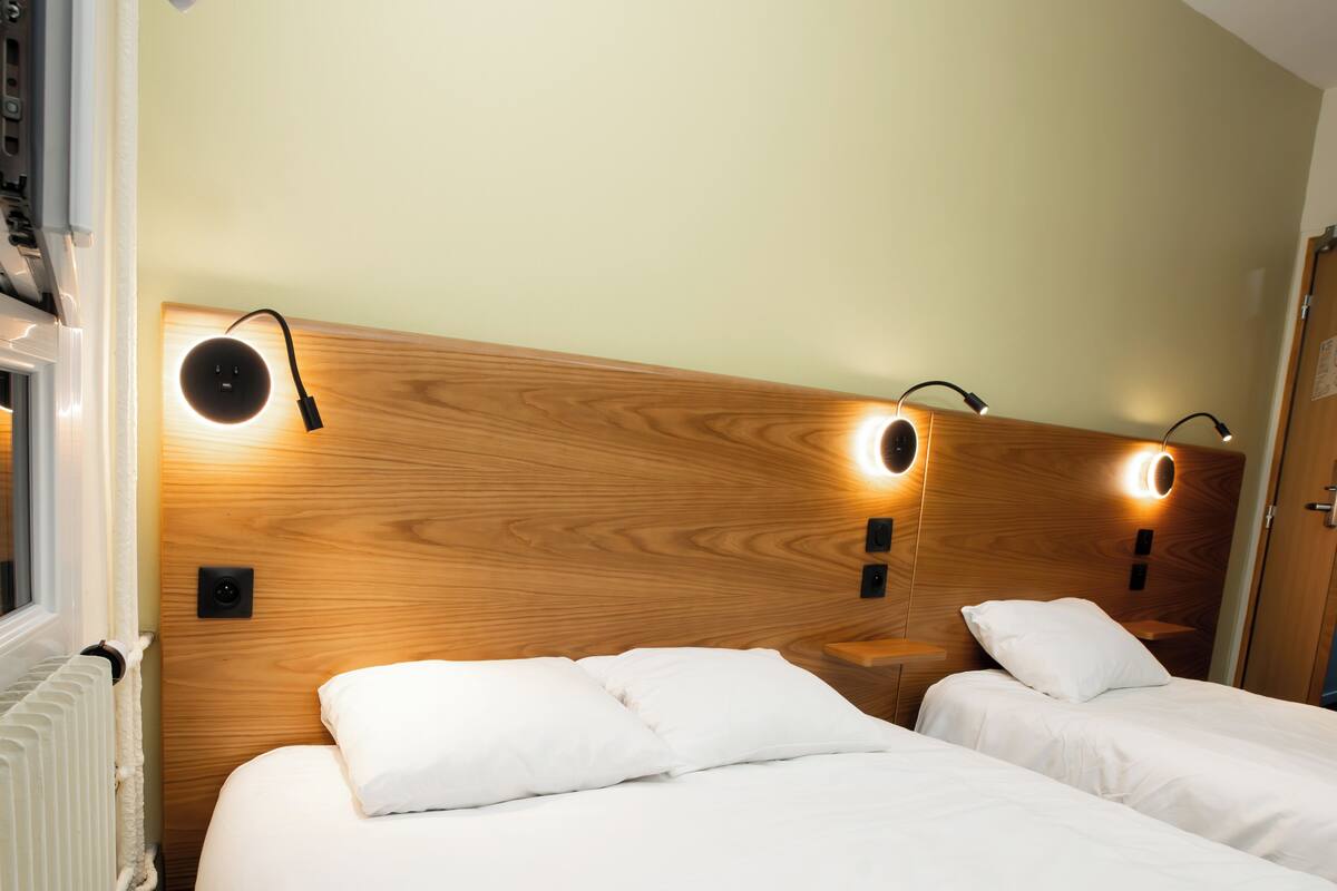 Une chambre d’hôtel avec deux lits, une tête de lit en bois et des lampes de lecture fixées au mur.