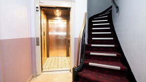 Un ascensor con piso de baldosas y una escalera con alfombra roja y barandilla.