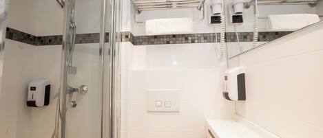 Une salle de bain moderne dotée d’une douche à parois de verre, d’un porte-serviettes avec plusieurs serviettes, d’un sèche-mains et d’un distributeur de savon.