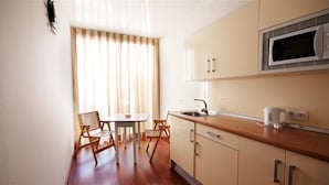 A compact kitchen with a microwave, sink, and wooden dining table with chairs. - Hotel Central (Marbella)