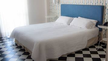 Een netjes opgemaakt bed met een blauw hoofdeinde, wit beddengoed en een geruit vloertje.