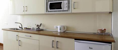 Una cocina compacta con microondas, cafetera y refrigerador pequeño.