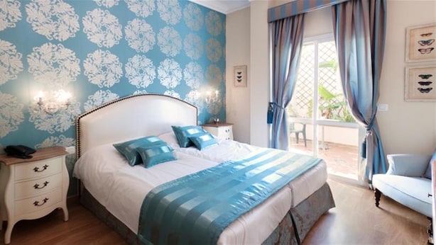 A bedroom with a large bed, a nightstand with a phone, and a chair. - Hotel Central (Marbella)