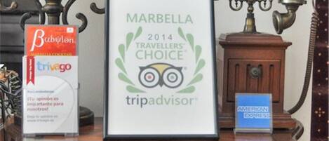 Un premio enmarcado, Travelers’ Choice de TripAdvisor para Marbella 2014, sobre un tocador de madera con dos cajones y una lámpara.
