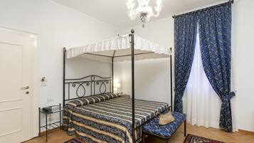 Un lit à baldaquin avec un ciel de lit blanc, un banc agrémenté d’un coussin à motifs, un lustre et un rideau à motifs.