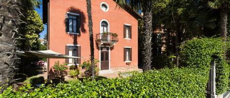 A red building with a balcony, surrounded by lush greenery and palm trees.