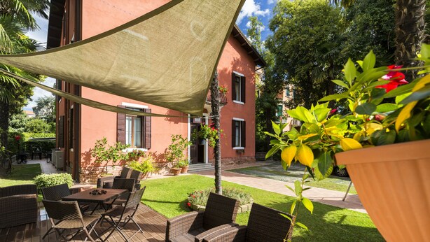 An outdoor patio with wicker furniture, a shaded area, and a building with red walls and windows. - Villa Casanova (Venice)
