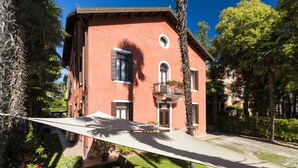 A red building with a balcony, surrounded by greenery and a clear sky. - Villa Casanova (Venice)
