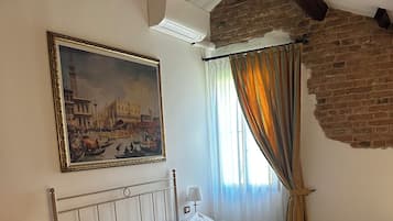 Une chambre d’hôtel avec un lit, un tableau, une fenêtre avec des rideaux et un mur en briques.