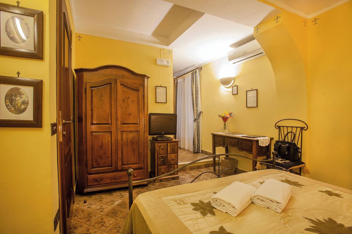 A hotel room with a bed, a wooden wardrobe, a television, a desk, and a chair.