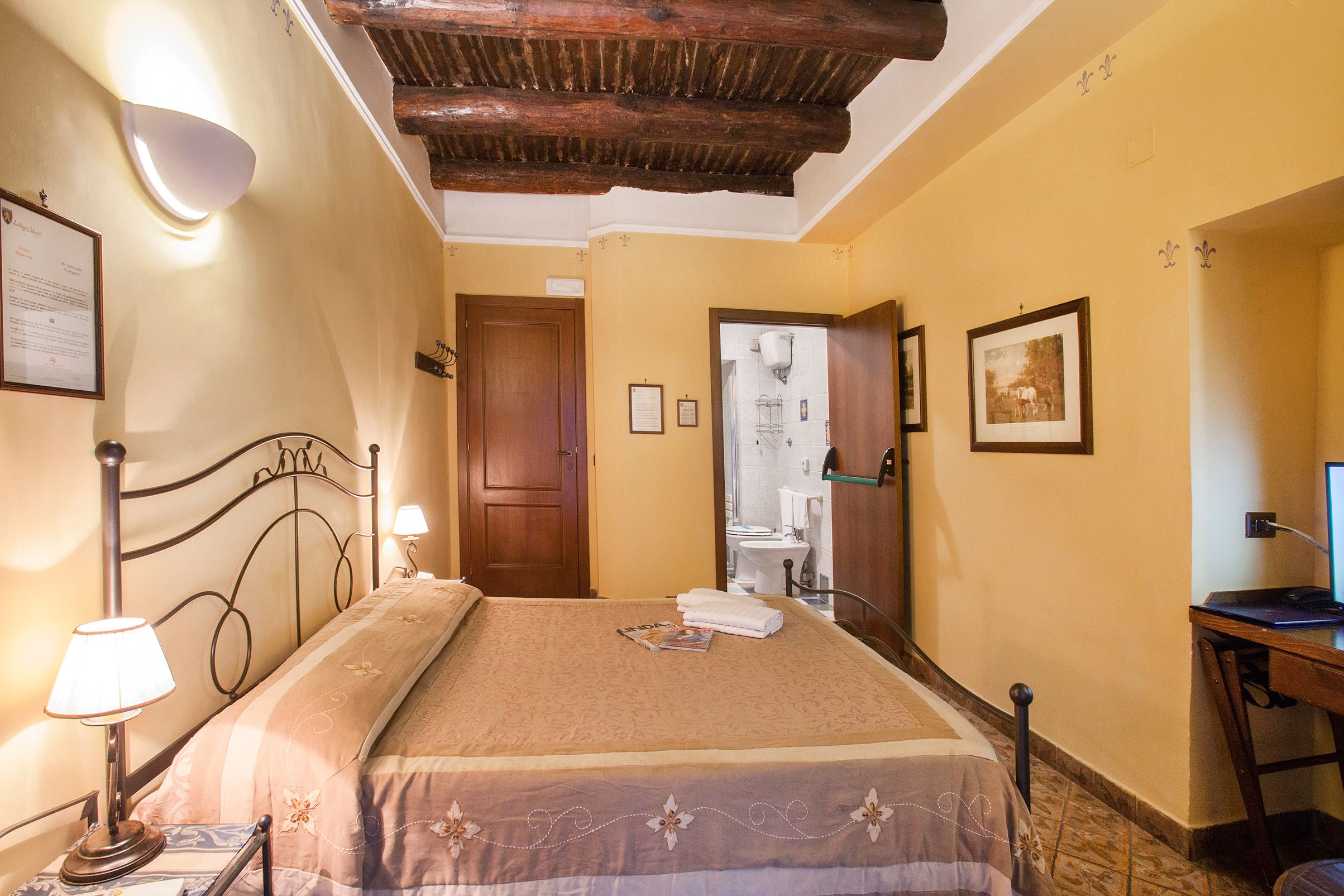 A hotel room with a bed, bedside lamps, a desk, and a wooden ceiling.