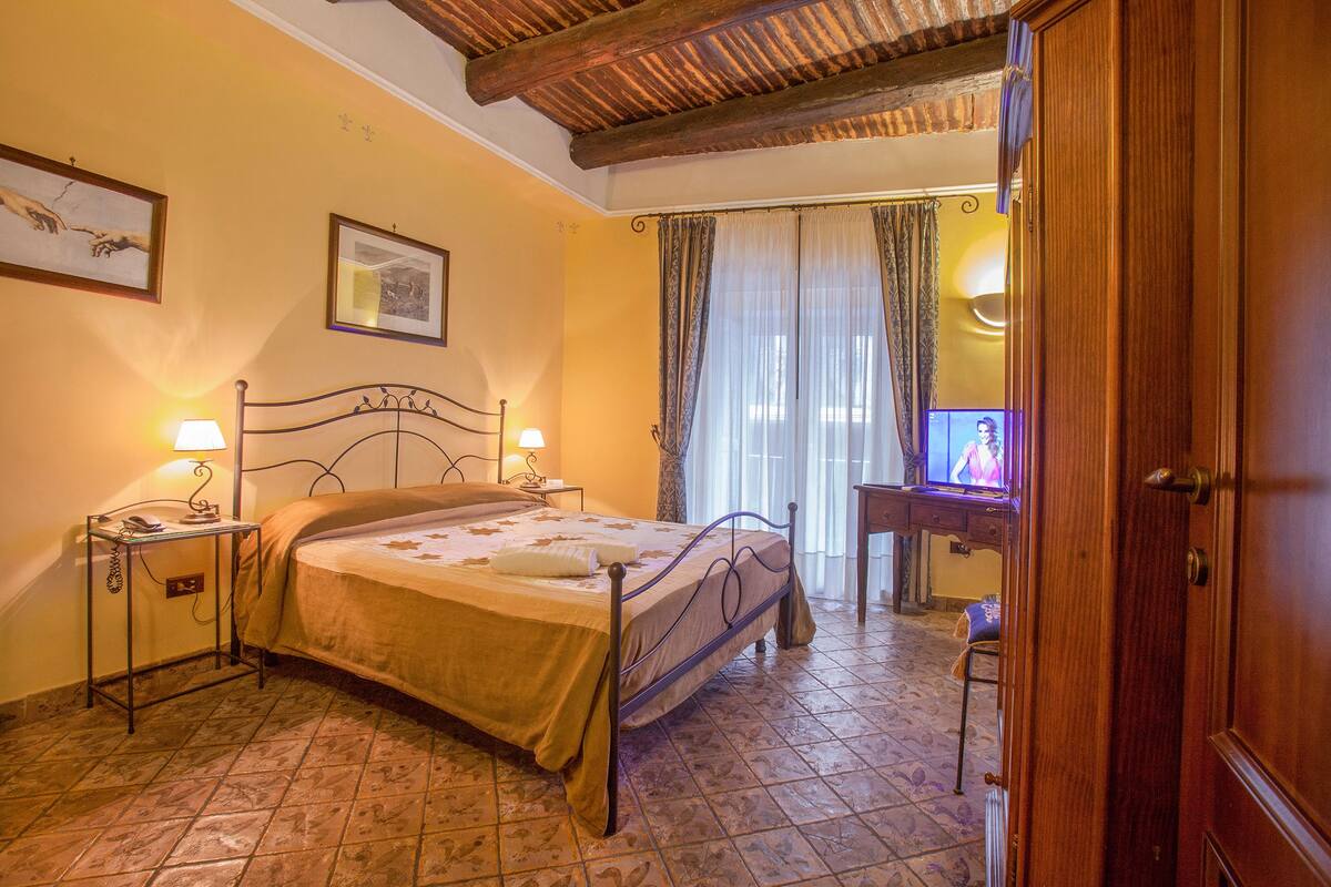 A bedroom with a bed, bedside tables, a wooden door, a mirror, and a television.