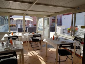 Un'area pranzo all'aperto coperta, con tavoli e sedie, ampie finestre e vista sulla strada.