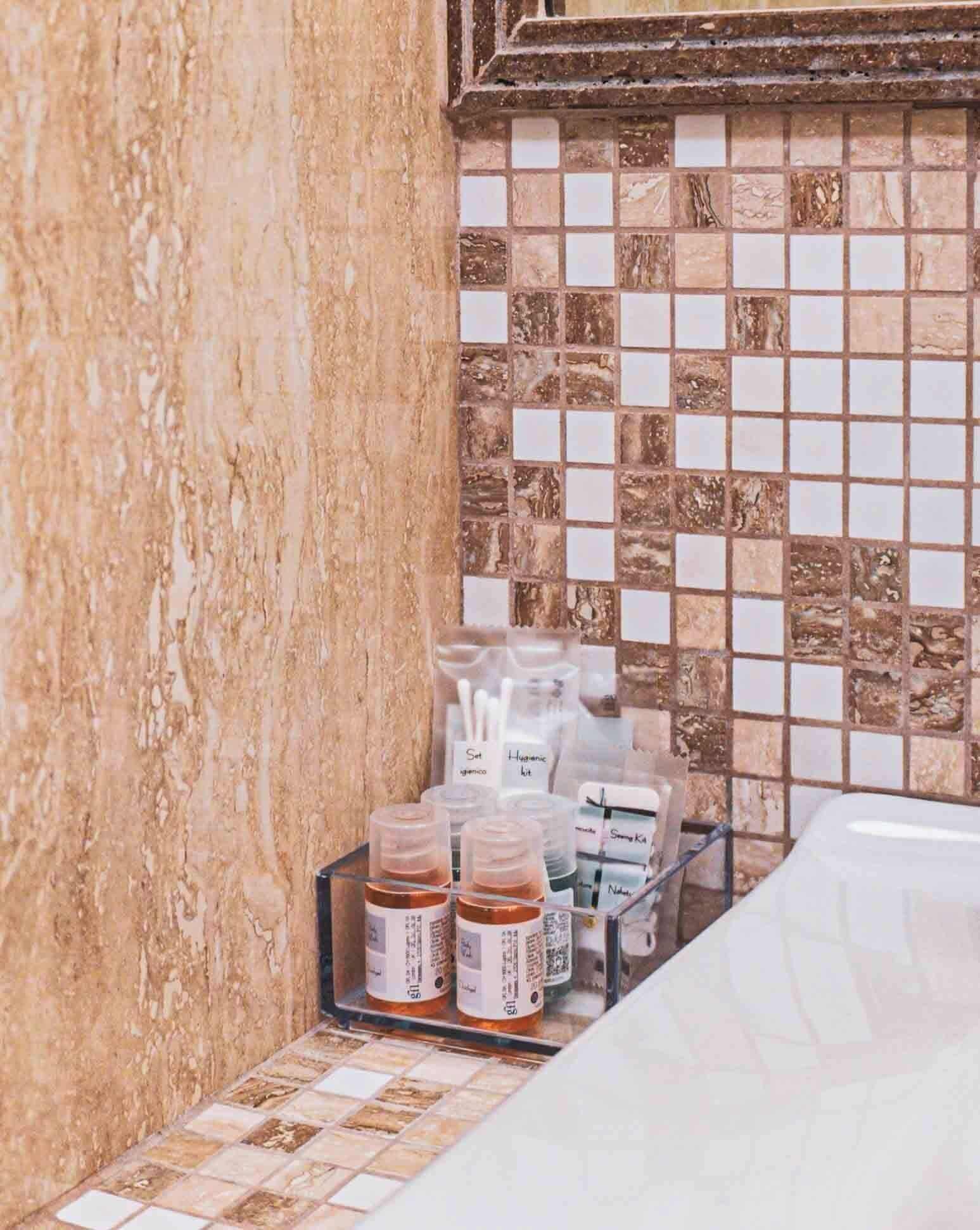 Un bagno con parete in marmo, rivestimento piastrellato e ripiano con flaconi da bagno.