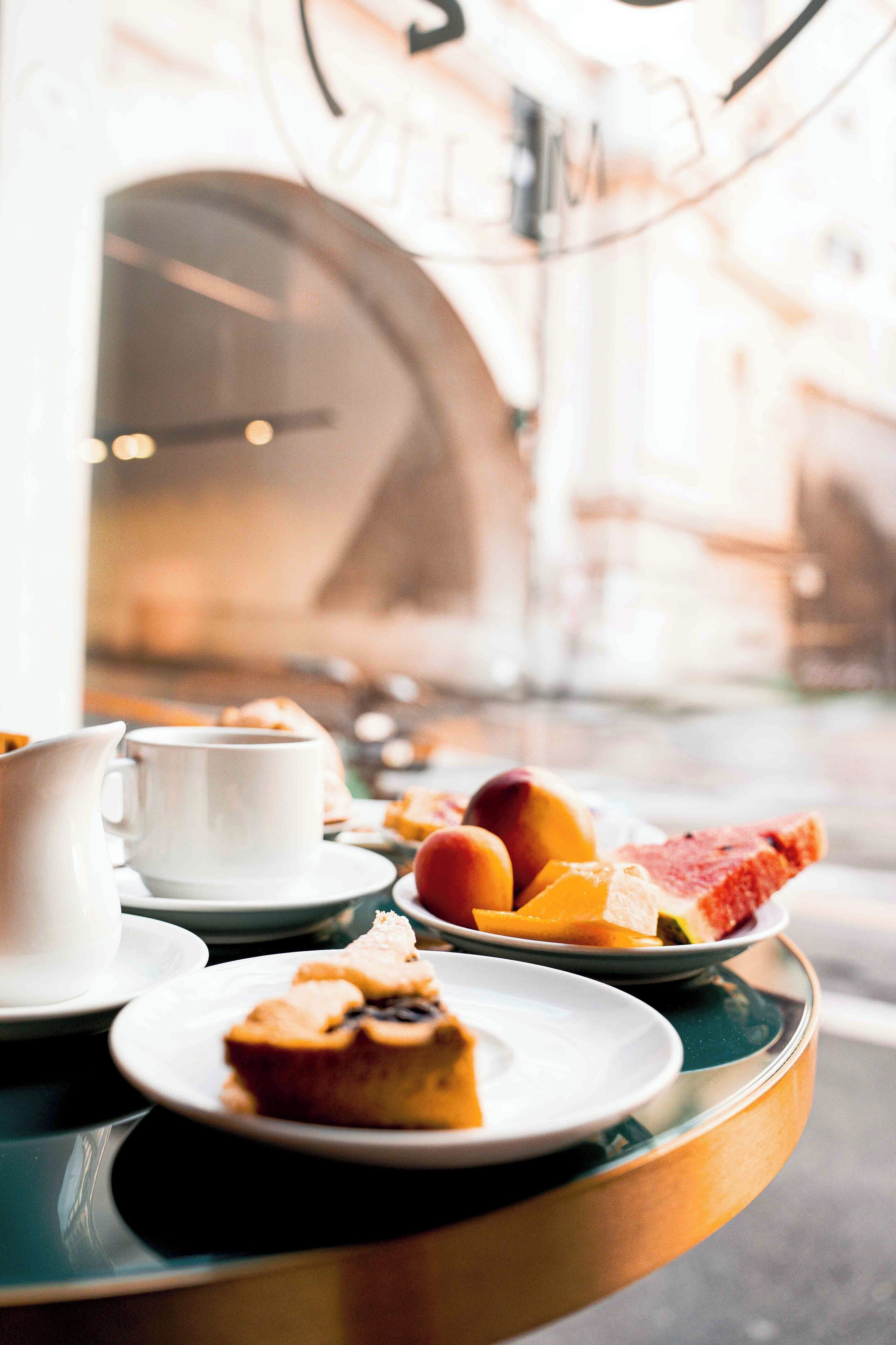 Une table avec une tasse blanche, un pichet et des assiettes contenant des pâtisseries et des fruits.