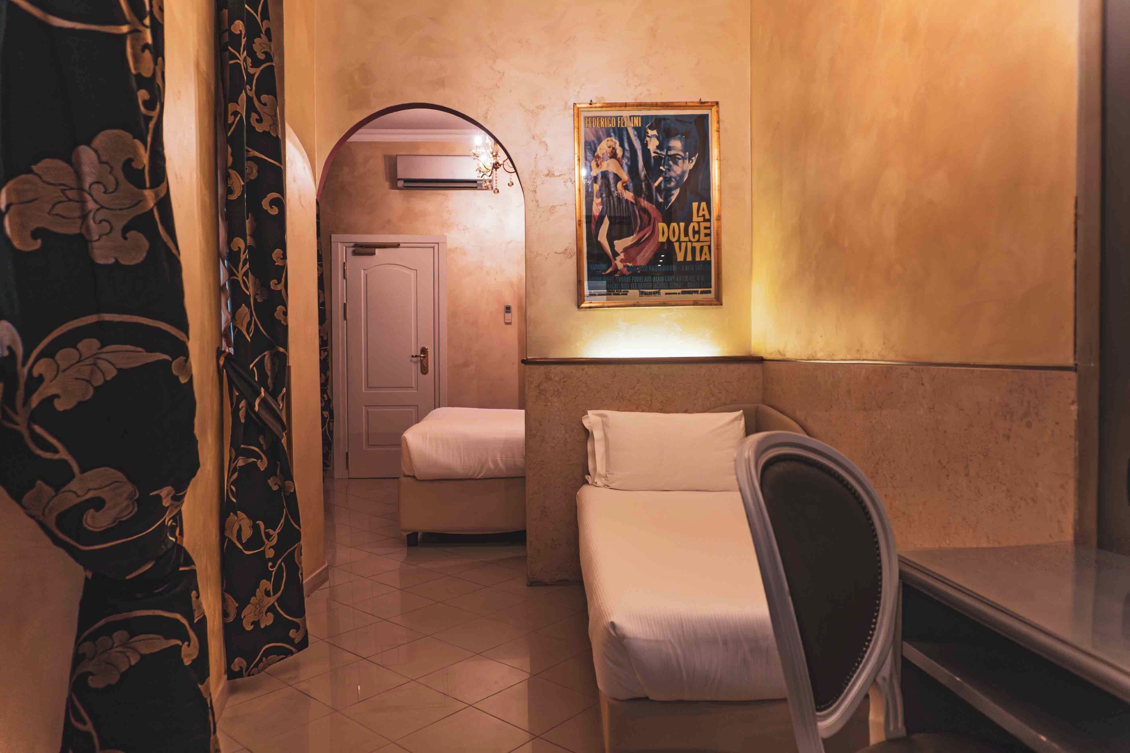 Una habitación de hotel con cama, una silla, un cartel en la pared y una puerta que da a otra habitación.