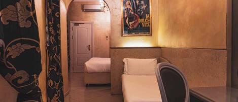 Una habitación de hotel con cama, una silla, un cartel en la pared y una puerta que da a otra habitación.