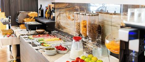 A buffet with various food items and beverages, a marble backsplash, and a window with a view.