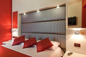 Une chambre d’hôtel moderne avec un grand lit, des oreillers rouges, un téléviseur fixé au mur et une table de chevet avec une télécommande.