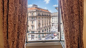 Een balkon met sierijzeren hekwerk, met uitzicht op een straat met gebouwen en een heldere lucht.